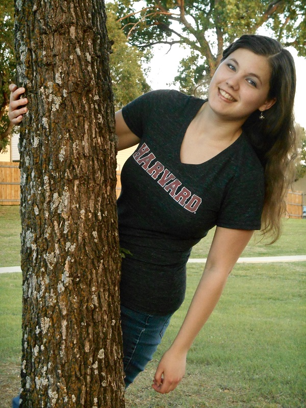 Livia leans out from behind a tree wearing a Harvard Tshirt